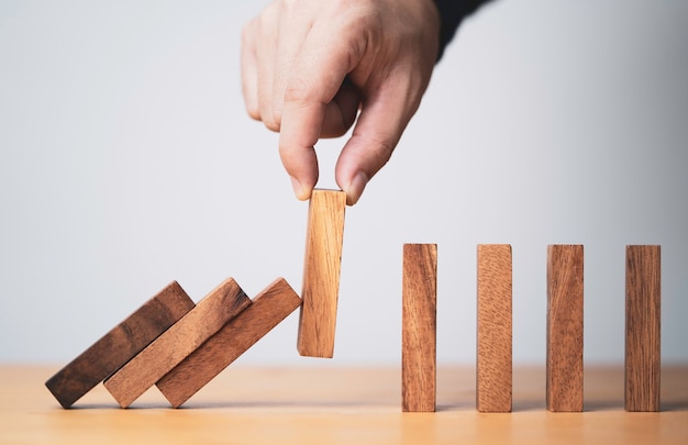 Extraiga el bloque de madera a mano para evitar y detener la caída del dominó, es un símbolo de protección contra daños o detener la pérdida para el concepto de gestión de crisis.