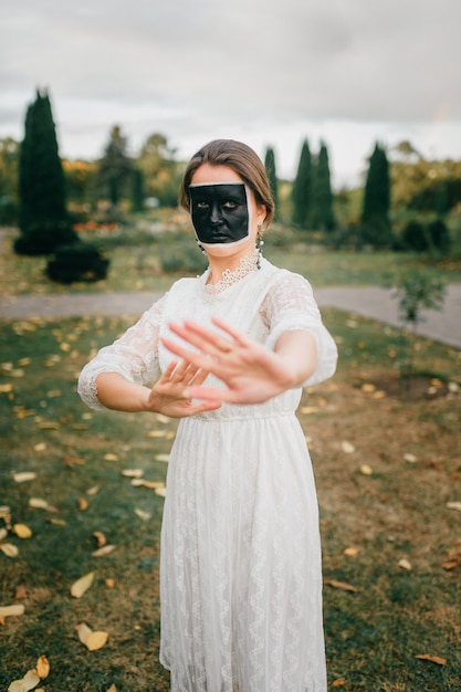 Extraña mujer en vestido de novia con cara creativa que muestra gestos con sus manos en el parque de verano