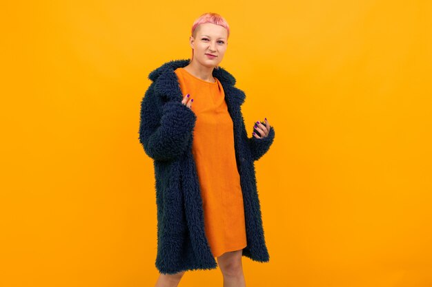 Extraordinaria mujer hermosa con cabello rosado corto en sonrisas de abrigo oscuro aislado sobre fondo naranja