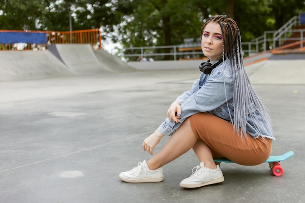 Extraordinaria patinadora milenaria con maquillaje colorido Trenzas africanas en un parque de patinaje Concepto de estilo de vida juvenil