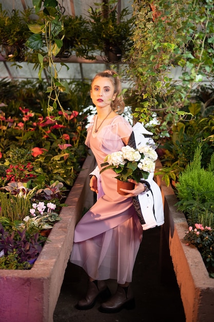 Extremamente bonito. Mulher bonita e elegante segurando uma flor branca em pé na estufa