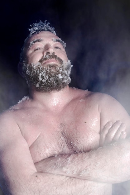 Extremo ruso un hombre desnudo en la nieve con barba congelada y cabello en las nubes de vapor