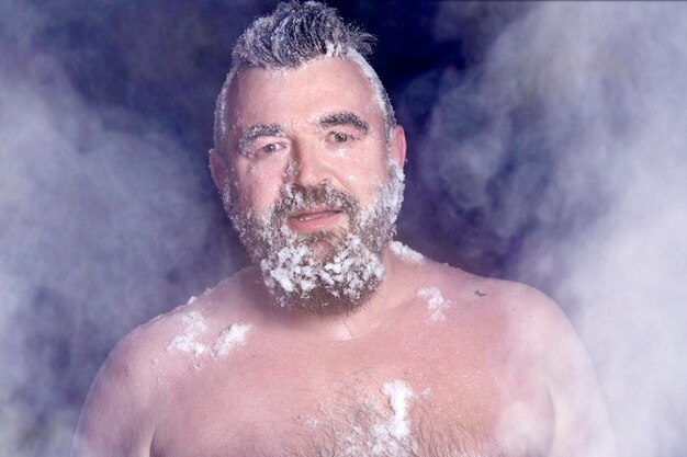 Extremo ruso un hombre desnudo en la nieve con barba congelada y cabello en las nubes de vapor