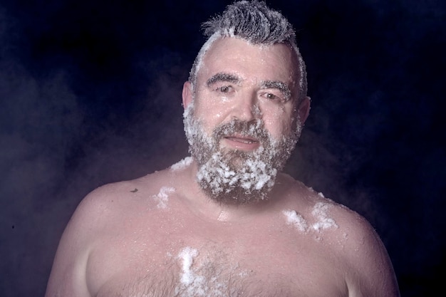 Extremo ruso un hombre desnudo en la nieve con barba congelada y cabello en las nubes de vapor