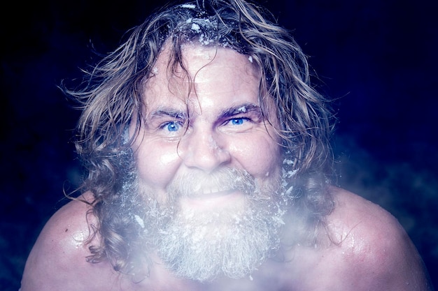 Extremo ruso un hombre desnudo en la nieve con barba congelada y cabello en las nubes de vapor