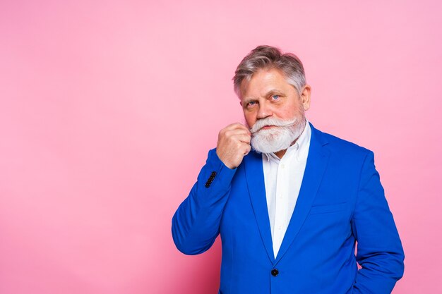 Exzentrischer älterer Mann mit blauem Blazer auf rosa Wand