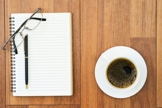 Eyeglasse und Notizblock mit Kaffeetasse auf hölzerner Plattform