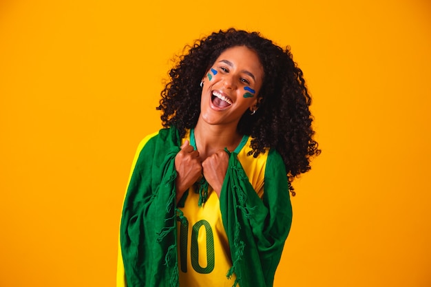 Fã brasileira. vestindo a bandeira brasileira em um retrato, fã brasileiro comemorando futebol ou jogo de futebol em fundo amarelo. Cores do Brasil. Copa do Mundo