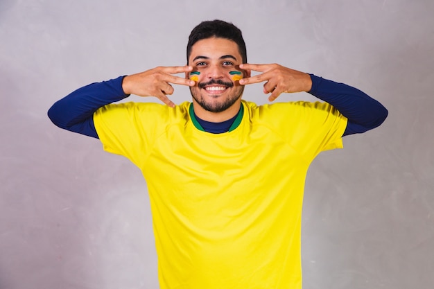 Fã brasileiro. usando tinta como maquiagem, fã brasileiro comemorando futebol ou jogo de futebol em fundo cinza. Cores do Brasil.