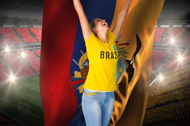 Fã de futebol animado em camiseta do brasil segurando a bandeira do equador contra um vasto estádio de futebol com fãs em amarelo e vermelho