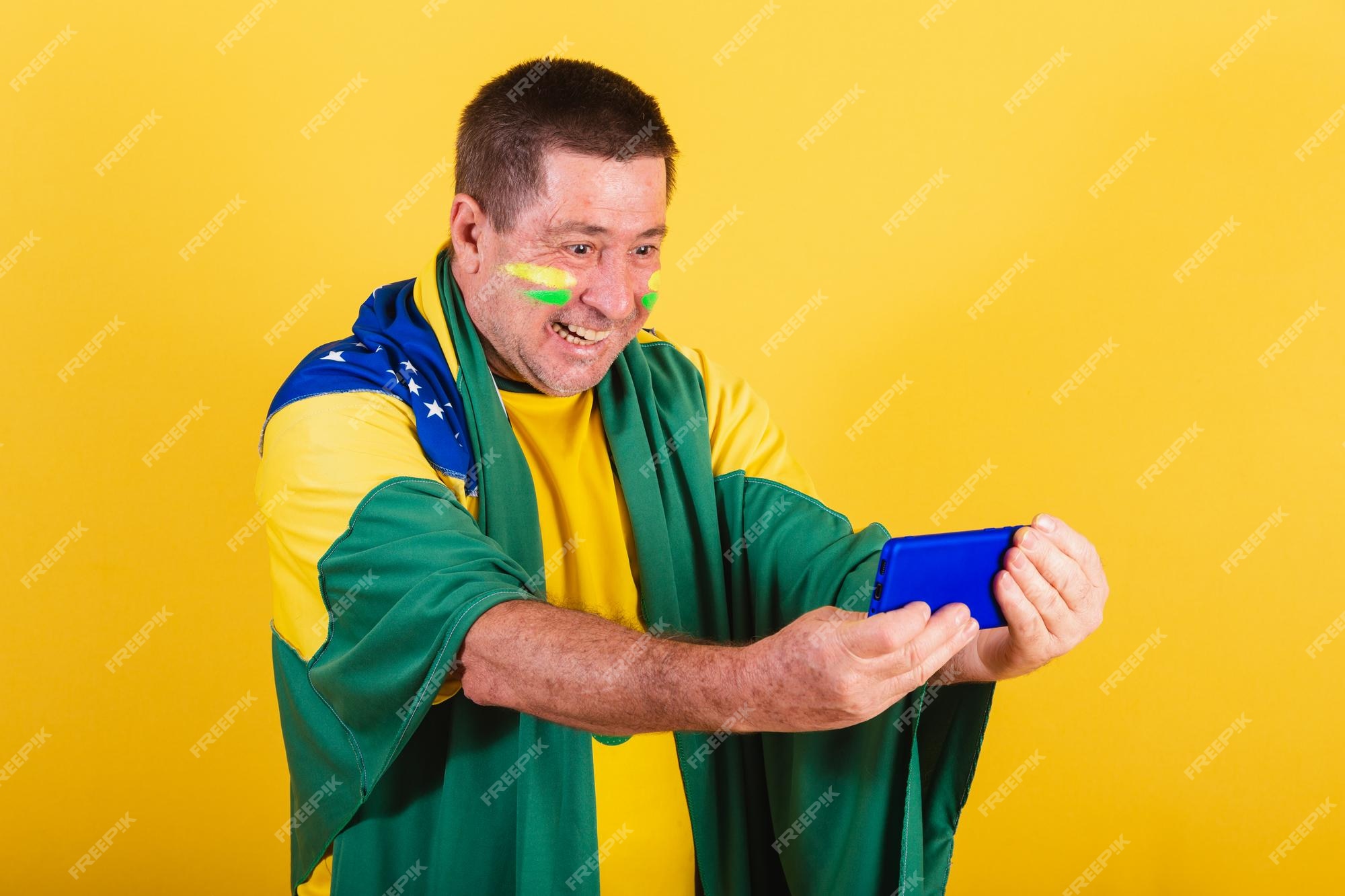 Fã de futebol brasileiro adulto usando smartphone de bandeira assistindo  jogo pelo celular streaming online