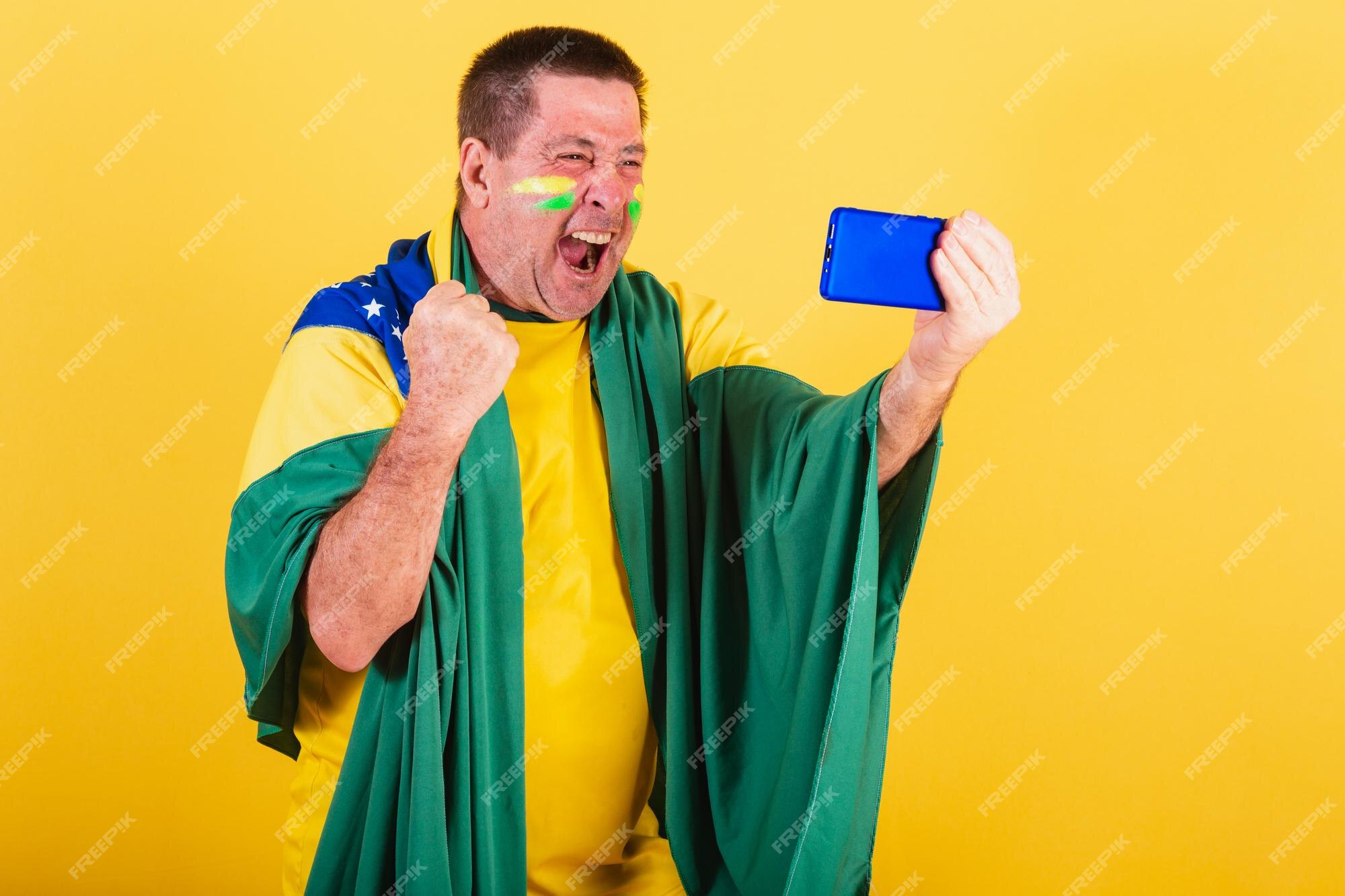 Fã de futebol brasileiro adulto usando smartphone de bandeira assistindo  jogo pelo celular streaming online