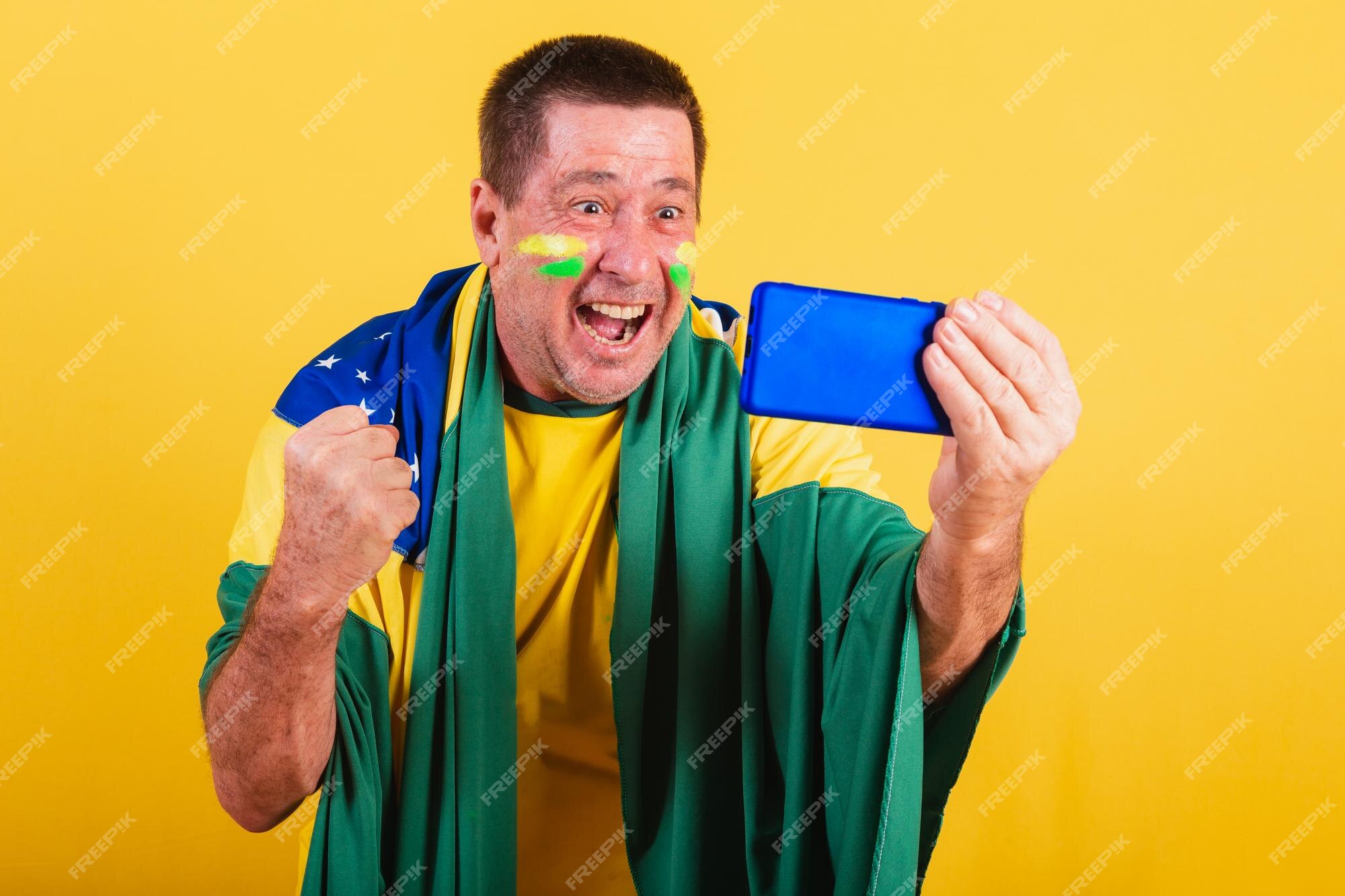 Fã de futebol brasileiro adulto usando smartphone de bandeira assistindo  jogo pelo celular streaming online