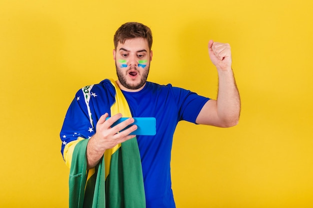 Fã de futebol brasileiro homem caucasiano do Brasil comemorando gol pelo celular