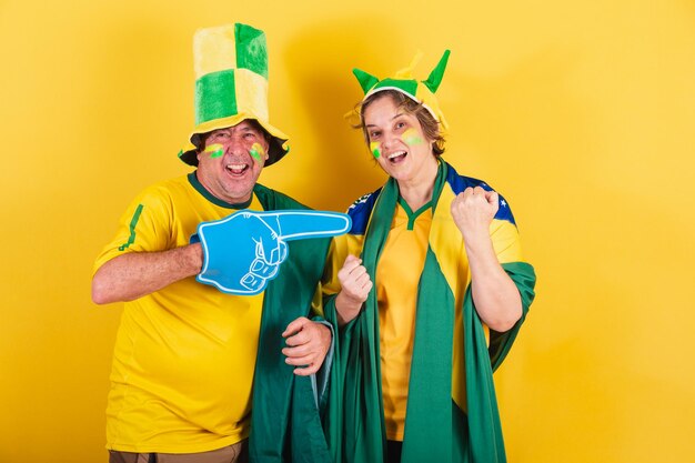 Fã de futebol de casal adulto do brasil usando bandeira e chapéu torcendo e festejando