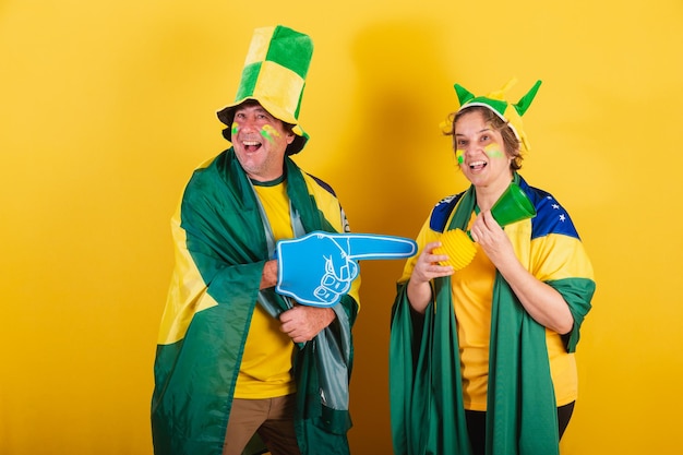 Fã de futebol de casal adulto do brasil usando bandeira e chapéu torcendo e festejando