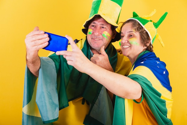 Fã de futebol de casal adulto do brasil usando videochamada de bandeira pelo aplicativo para smartphone foto de publicidade móvel