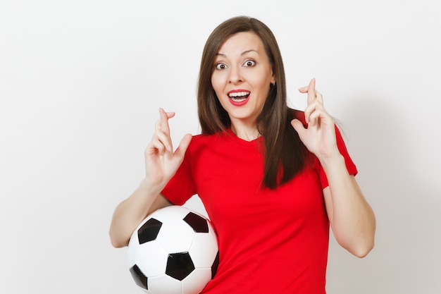 Fã de futebol europeu jovem ou jogador com uniforme vermelho, manter os dedos cruzados segura uma bola de futebol isolada no fundo branco. O esporte joga o conceito de estilo de vida do futebol. Aguarde um momento especial. Faça desejo