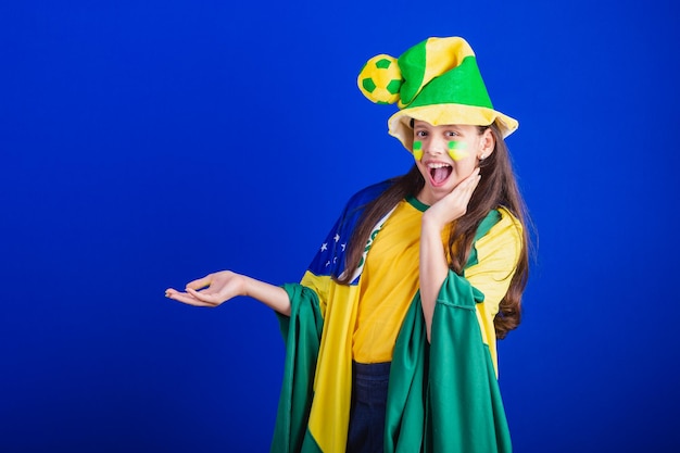 Fã de futebol jovem do Brasil vestido de chapéu e bandeira apresentando algo