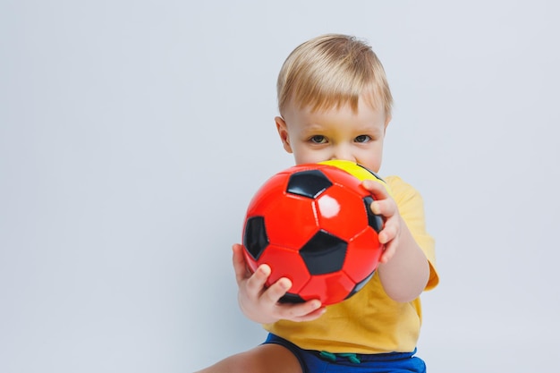 Fã de menino europeu ou jogador de uniforme amarelo e azul com uma bola de futebol apoia o time de futebol em um fundo branco Conceito de estilo de vida de jogo de esporte de futebol isolado no fundo branco