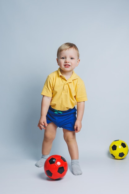 Fã de menino segurando uma bola de futebol nas mãos isoladas em um fundo branco criança novato no esporte de futebol para crianças Atleta pequeno Kit de futebol amarelo e azul para crianças