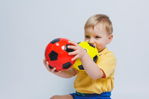 Fã de menino segurando uma bola de futebol nas mãos isoladas em um fundo branco criança novato no esporte de futebol para crianças atleta pequeno kit de futebol amarelo e azul para crianças