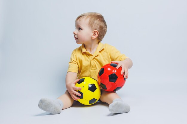 Fã de menino segurando uma bola de futebol nas mãos isoladas em um fundo branco criança novato no esporte de futebol para crianças Atleta pequeno Kit de futebol amarelo e azul para crianças