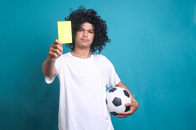 Fã de suporte de futebol com peruca de cabelo encaracolado segurando bola de futebol e cartão de árbitro amarelo