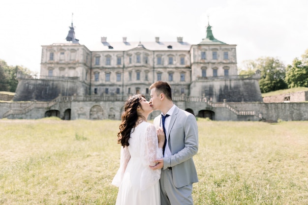 Fabelhaftes asiatisches Hochzeitspaar, das vor einer alten mittelalterlichen Burg aufwirft, an einem sonnigen Tag umarmt und küsst.