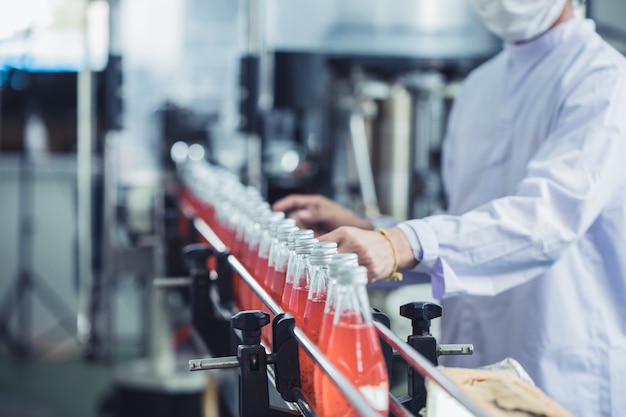 Fábrica de bebidas - primer trabajador de higiene trabajando vidrio de jugo de verificación embotellado en la línea de producción