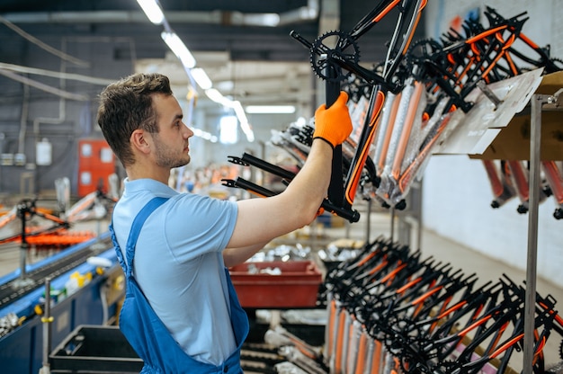 Fábrica de bicicletas, trabalhador na linha de montagem de bicicletas. Mecânico masculino em uniforme instala peças de ciclo na oficina