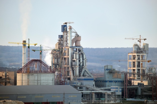 Fábrica de cimento com estrutura fabril alta e guindastes de torre na área de produção industrial. Manufatura, indústria global e conceito de poluição do ar