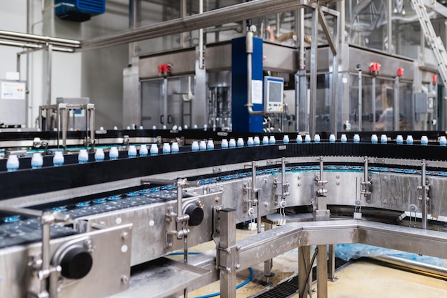 Fábrica de engarrafamento - linha de engarrafamento de água para processamento e engarrafamento de água pura em garrafas azuis. Foco seletivo.