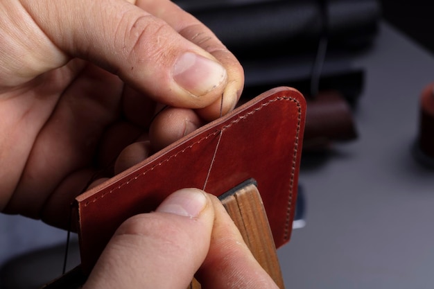 Fabricación de carteras de cuero Las manos del maestro cosen un producto de cuero.