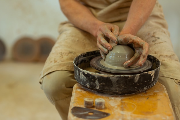 Fabricación de macetas nuevas. Hombre fuerte calificado con las manos sucias y mojadas produciendo en torno de alfarería mientras permanece en el estudio