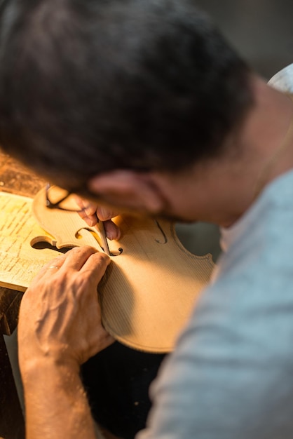 Fabricante de violino trabalhando e cortando buracos em uma mesa de violino