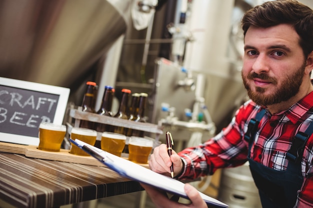 Fabricante escrevendo enquanto examina cerveja em cervejaria