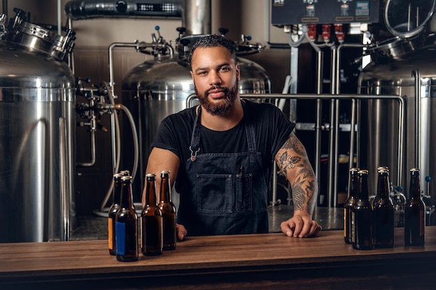 Fabricante masculino hipster tatuado de barba preta apresentando cerveja artesanal na microcervejaria.