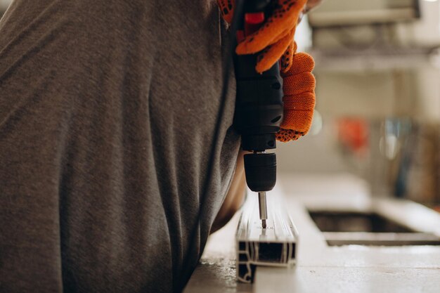 Fabrik für die Herstellung von Aluminium- und PVC-Fenstern und -Türen Arbeiter, der PVC-Türen und -Fenster zusammenbaut und mit einer Schraubpistole arbeitet