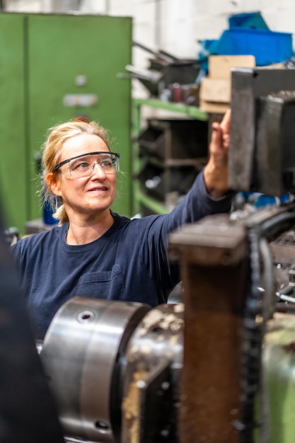 Fabrikarbeiterin, die im Kontrollbereich einer Industriefabrik für Metallfräsmaschinen arbeitet