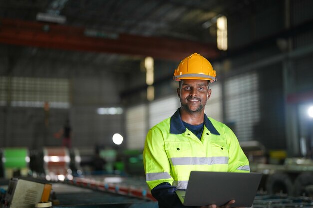 Fabrikingenieur Afrikanischer Mann steht selbstbewusst mit Laptop Arbeiter arbeitet an schwerer Maschine in Industriefabrik mit Maschinenausrüstung Anlagentechnik