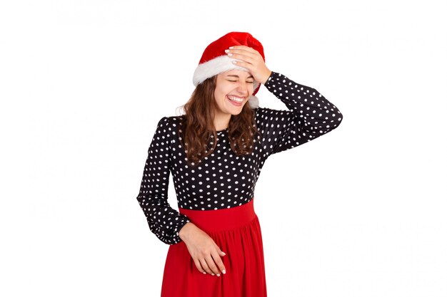 Foto fabulosa mujer alegre mostrando la lengua y mirando hacia abajo risas puso la mano en la frente. chica emocional en santa claus sombrero de navidad aislado