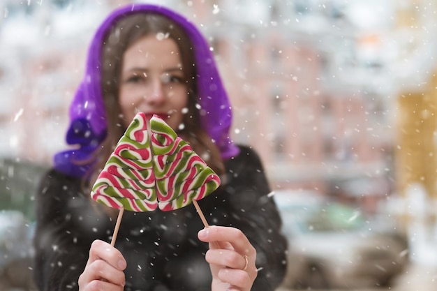 Fabulosa mujer morena divirtiéndose con paletas de colores en la calle con copos de nieve. Espacio para texto