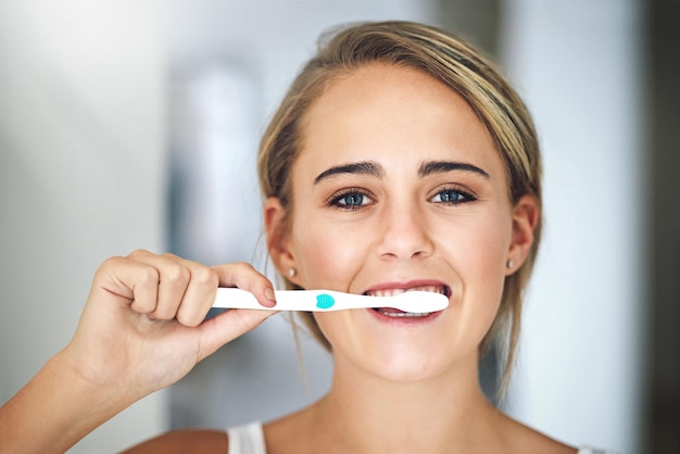 Faça da boa higiene um hábito Retrato de uma jovem atraente escovando os dentes no banheiro