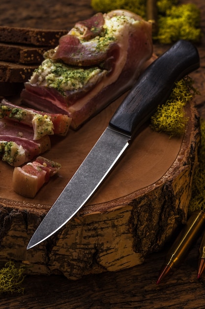 Foto faca de caça de damasco perto de bacon fatiado em fundo de madeira