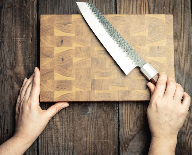 Foto faca de cozinha de metal e tábua de madeira em uma mesa feita de tábuas de madeira marrom, vista superior