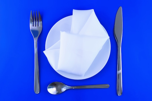 Foto faca de servir de mesa, prato, garfo e guardanapo de seda sobre fundo de cor azul.