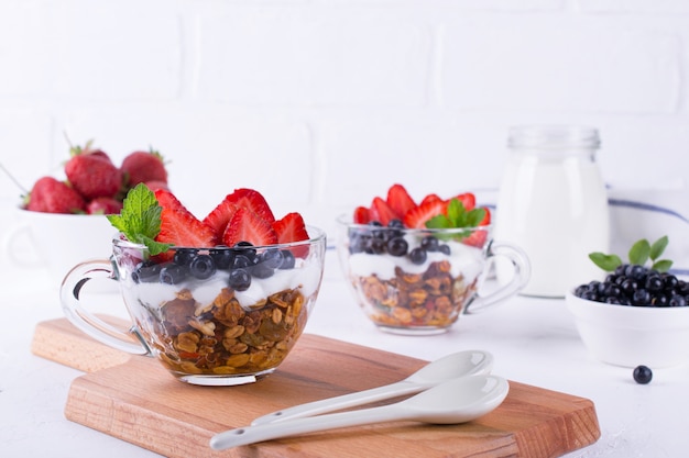 Faça dieta a sobremesa saudável com iogurte, granola e frutas frescas. no fundo da mesa branca