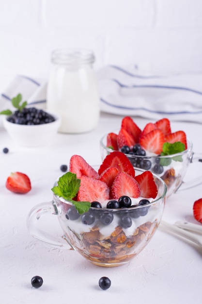 Faça dieta a sobremesa saudável com iogurte, granola e frutas frescas. no fundo da mesa branca