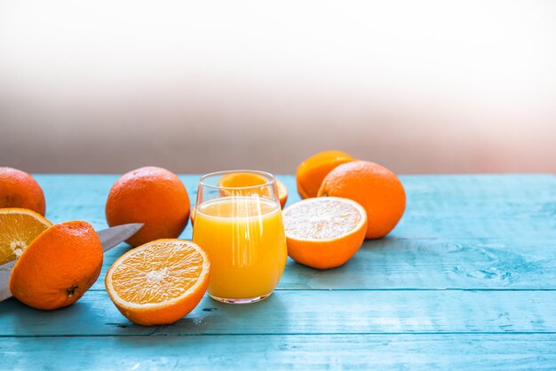 Faca dividindo uma laranja ao meio, copo de suco natural de várias laranjas orgânicas, algumas inteiras, algumas espremidas, para a dieta, em uma mesa de madeira azul, café da manhã saudável